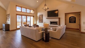 A spacious living room with high ceilings, large windows, a fireplace, and a television. - On the Rocks (Banner Elk)