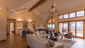 A spacious living area with a large sofa, a coffee table, and a dining area with chairs and a kitchen in the background. - On the Rocks (Banner Elk)