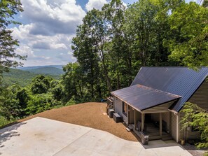 A cabin with a sloped roof, a porch, and a view of a forested landscape.