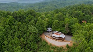 A cabin surrounded by dense forest with a view of distant mountains. - Skyline Escape Stunning Long Range Views, Hot Tub, Firepit, Lawn Games (Lenoir)