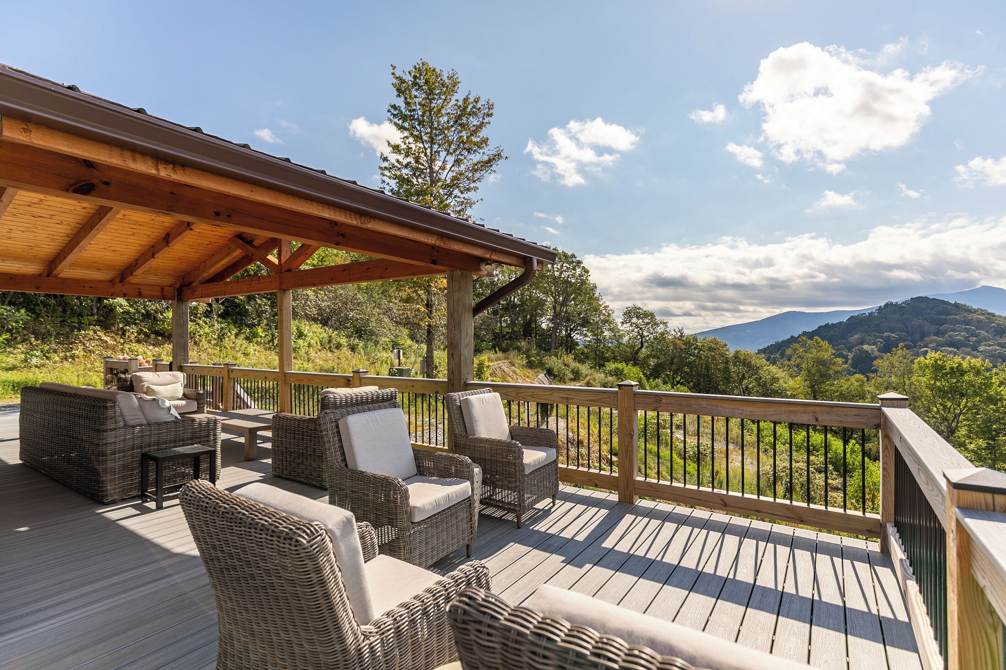 Une terrasse en bois, meublée de mobilier en osier, offrant une vue sur un paysage montagneux.
