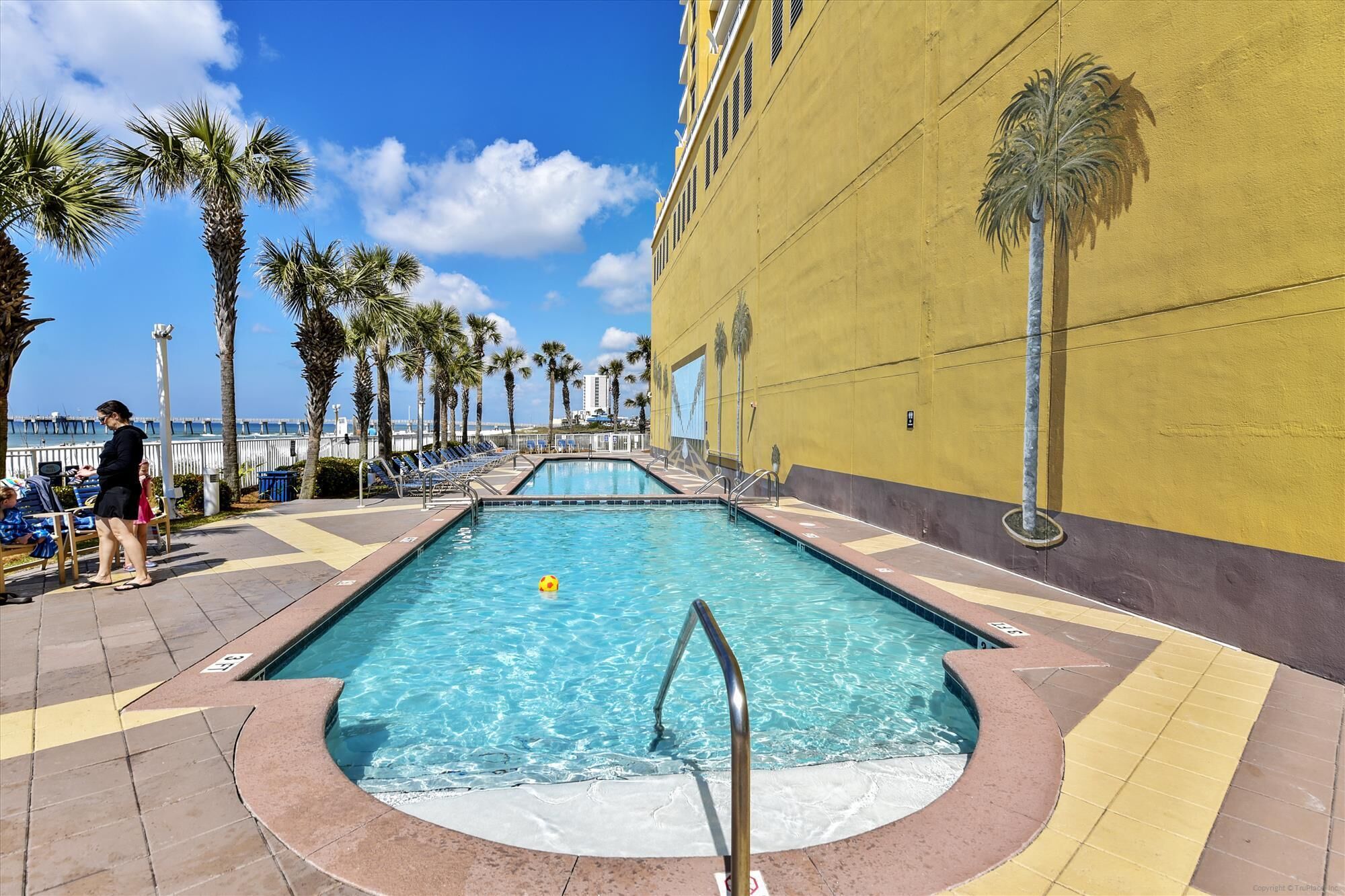 A pool area with two pools, lounge chairs, and palm trees.