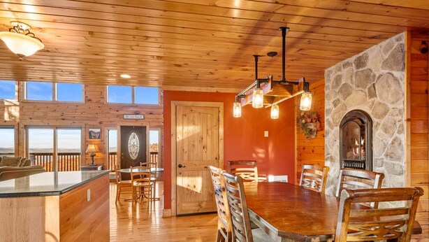 A wooden interior with a stone fireplace, a dining area with a wooden table and chairs, and a bar area with a glass-top table. - Beech Mountain Breeze - Views, pet Friendly, hot Tub, Sleeps 14 (Banner Elk)