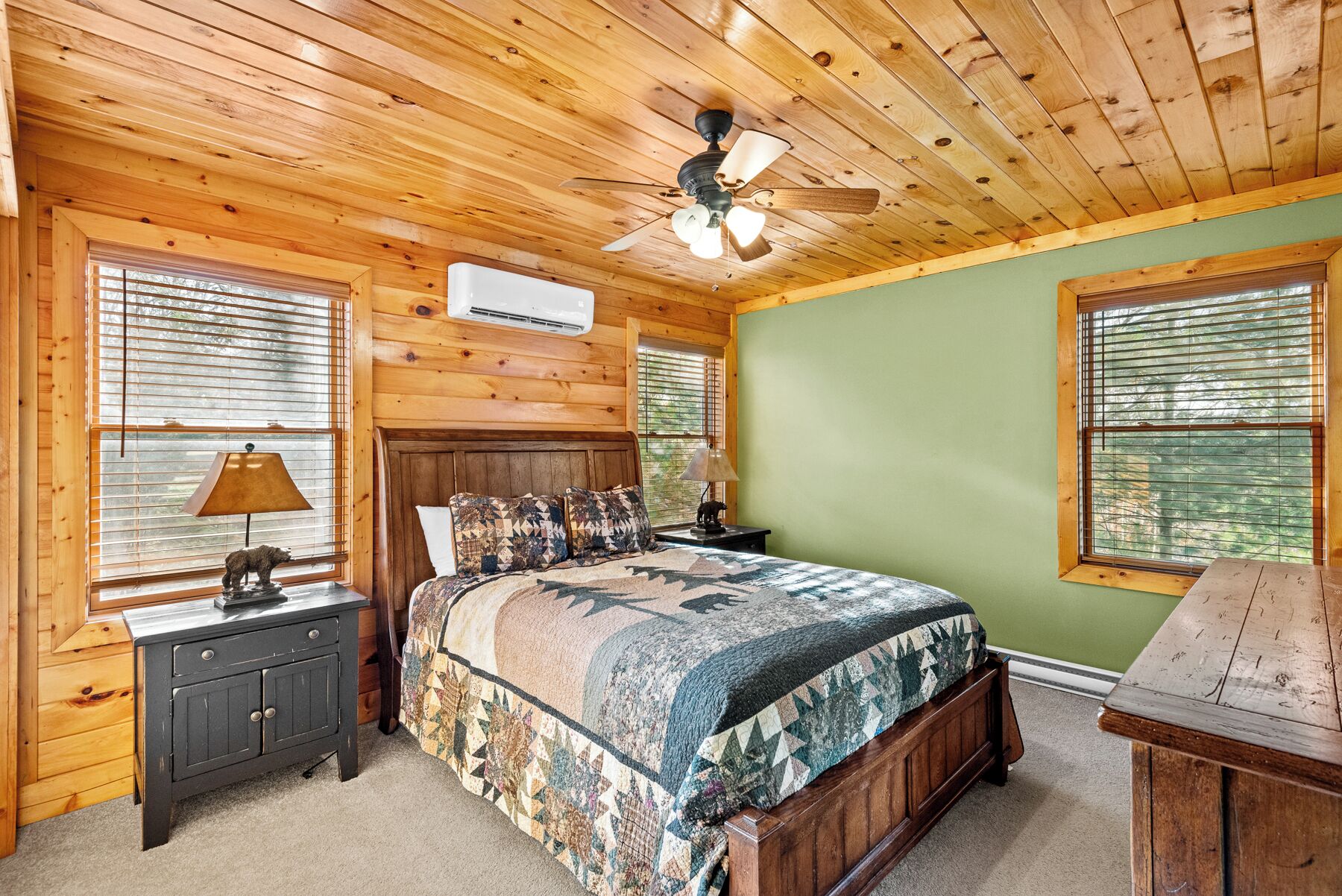 A wooden cabin bedroom with a bed, nightstands, a ceiling fan, and large windows.