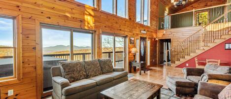 A spacious living room with a large sofa, a coffee table, and a view of the mountains through large windows.