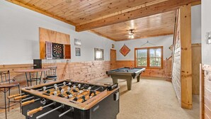 A room with a foosball table, pool table, dartboard, and a window with a view of trees. - Beech Mountain Breeze - Views, pet Friendly, hot Tub, Sleeps 14 (Banner Elk)