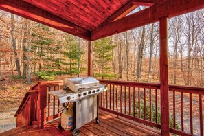 Ein überdachter Grillbereich im Freien mit Gasflasche und mehreren Brennern, vor einer bewaldeten Landschaft.