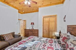 Ein Schlafzimmer mit Holzboden, einem Bett mit gemustertem Überwurf, einem Holzschrank, einem Holzgarderobe und einer hölzernen Sitzbank.
