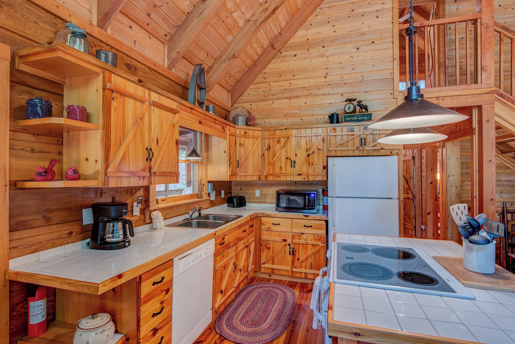 A wooden cabin kitchen with a stove, microwave, sink, and wooden cabinets.
