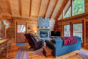 A cozy cabin interior with a stone fireplace, wooden walls, a comfortable sofa, and a television. - Bucks Cabin - Minutes From Downtown, pet Friendly (Boone)