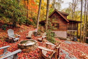 A cabin with a stone fire pit, wooden chairs, and a wooden deck. - Bucks Cabin - Minutes From Downtown, pet Friendly (Boone)