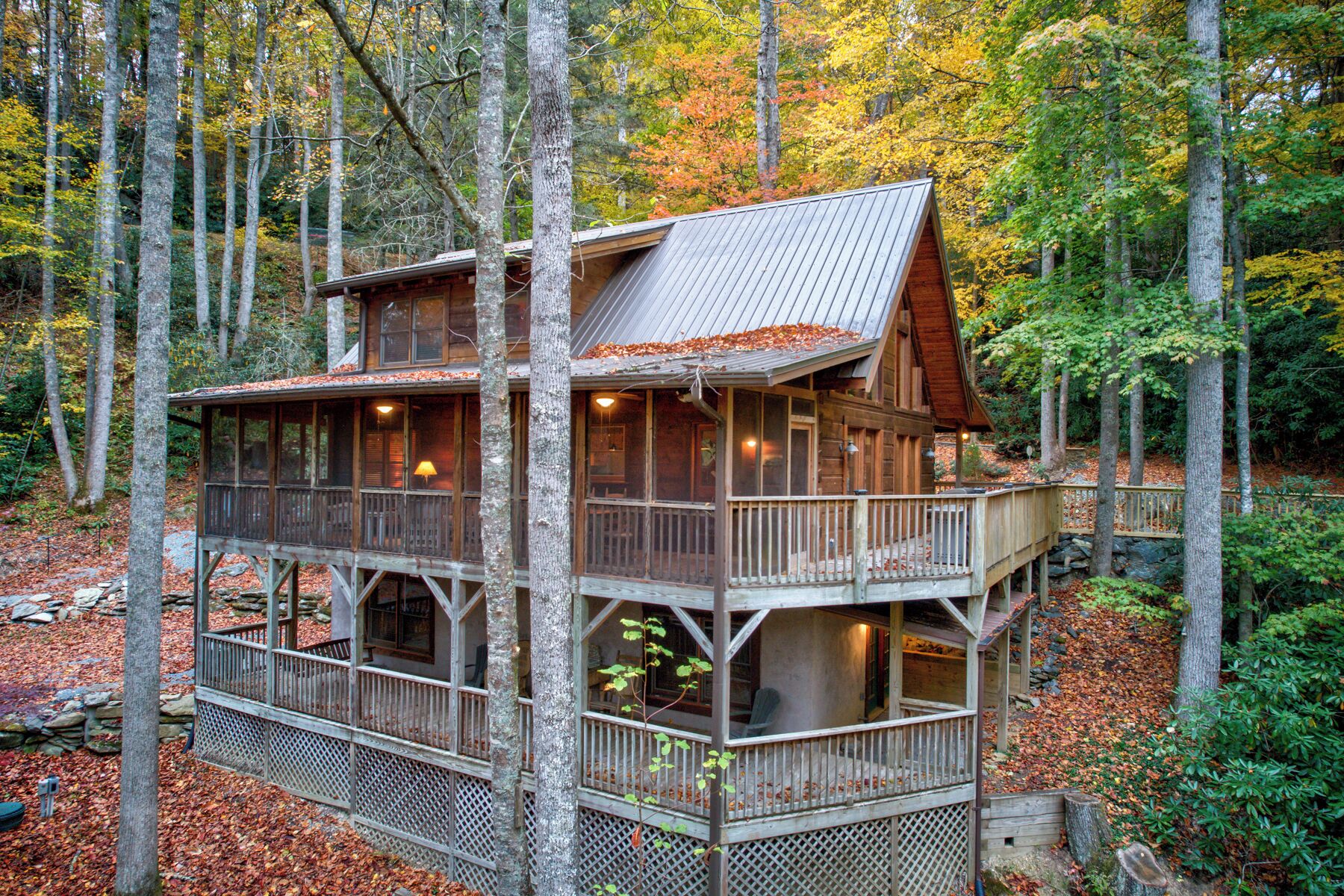 A two-story wooden cabin with a balcony, surrounded by a forest.
