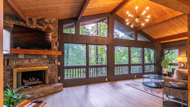 A spacious living room with a stone fireplace, large windows, and a wooden ceiling. - Blue Ridge Retreat at Linville Land Harbor (Newland)