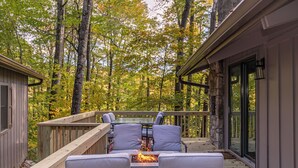 A deck with outdoor seating and a fire feature, surrounded by trees. - Blue Ridge Retreat at Linville Land Harbor (Newland)