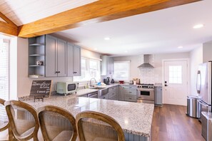 A modern kitchen with granite countertops, built-in cabinets, a central island, and a dining area with wicker chairs. - Stella Maris - own Blowing Rock Pet Friendly Updated Craftsman Bungalow (Blowing Rock)