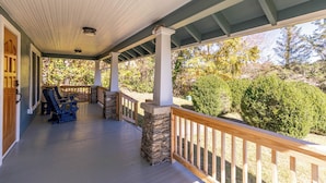 Eine überdachte Veranda mit steinernen Säulen, Holzgeländern und blauen Adirondack-Stühlen.