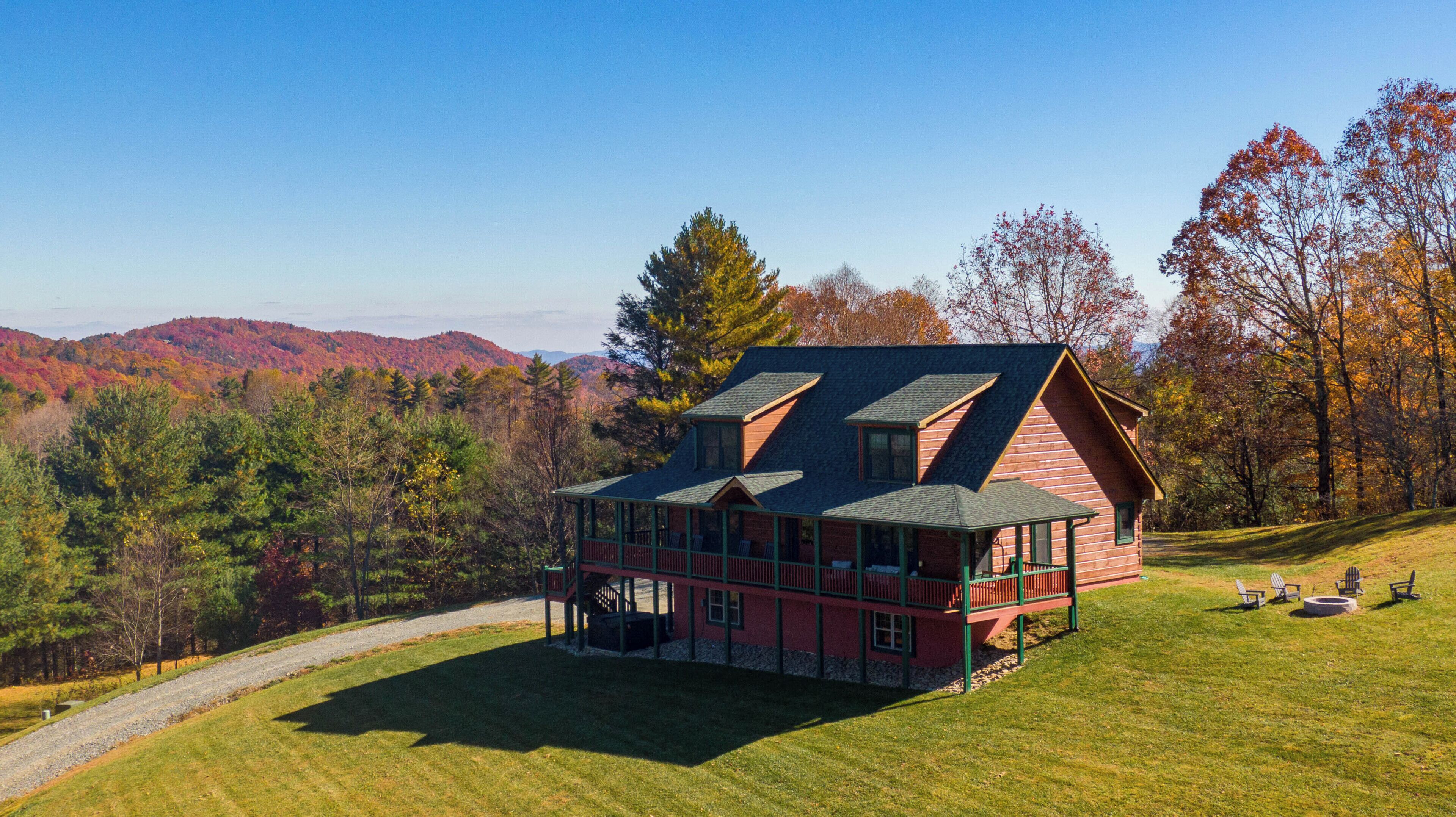 A log cabin with a steep roof, a porch, and a view of a mountainous landscape.