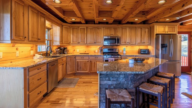 A spacious kitchen with wooden cabinets, granite countertops, a stone island, and a built-in refrigerator. - Good Medicine (Boone)
