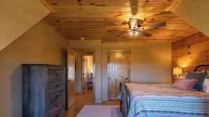 A bedroom with a wooden ceiling, a bed with patterned bedding, a dresser, and a ceiling fan. - Good Medicine (Boone)
