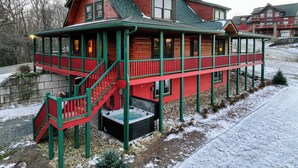 A log cabin with a porch, a hot tub, and a staircase leading to the entrance. - Good Medicine (Boone)
