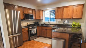 A modern kitchen with wooden cabinets, stainless steel appliances, a microwave, and a small island with stools.