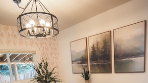 A dining area with a wooden table, black chairs, a chandelier, and three landscape paintings on the wall.