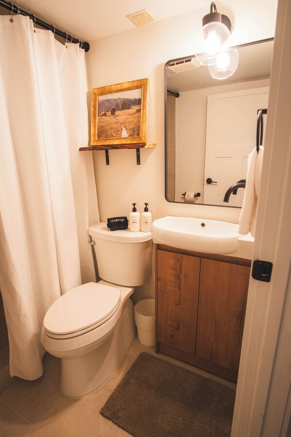 A bathroom with a toilet, sink, mirror, and a framed picture on the wall.