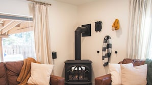 A cozy living room with two brown leather sofas, a round wooden coffee table, and a black wood-burning stove.