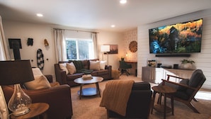 A living room with a sofa, armchair, coffee table, and a television mounted on the wall.
