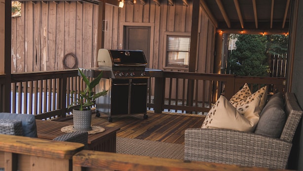 A wooden deck with a grill, wicker furniture, and a view of trees.