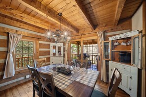 A wooden cabin interior with a dining table, chairs, a chandelier, a coffee bar, and a view through a window. - 5 Bears Cabin Wooded Cabin With hot Tub, Arcade Games, Pool Table, Fire pit (Banner Elk)