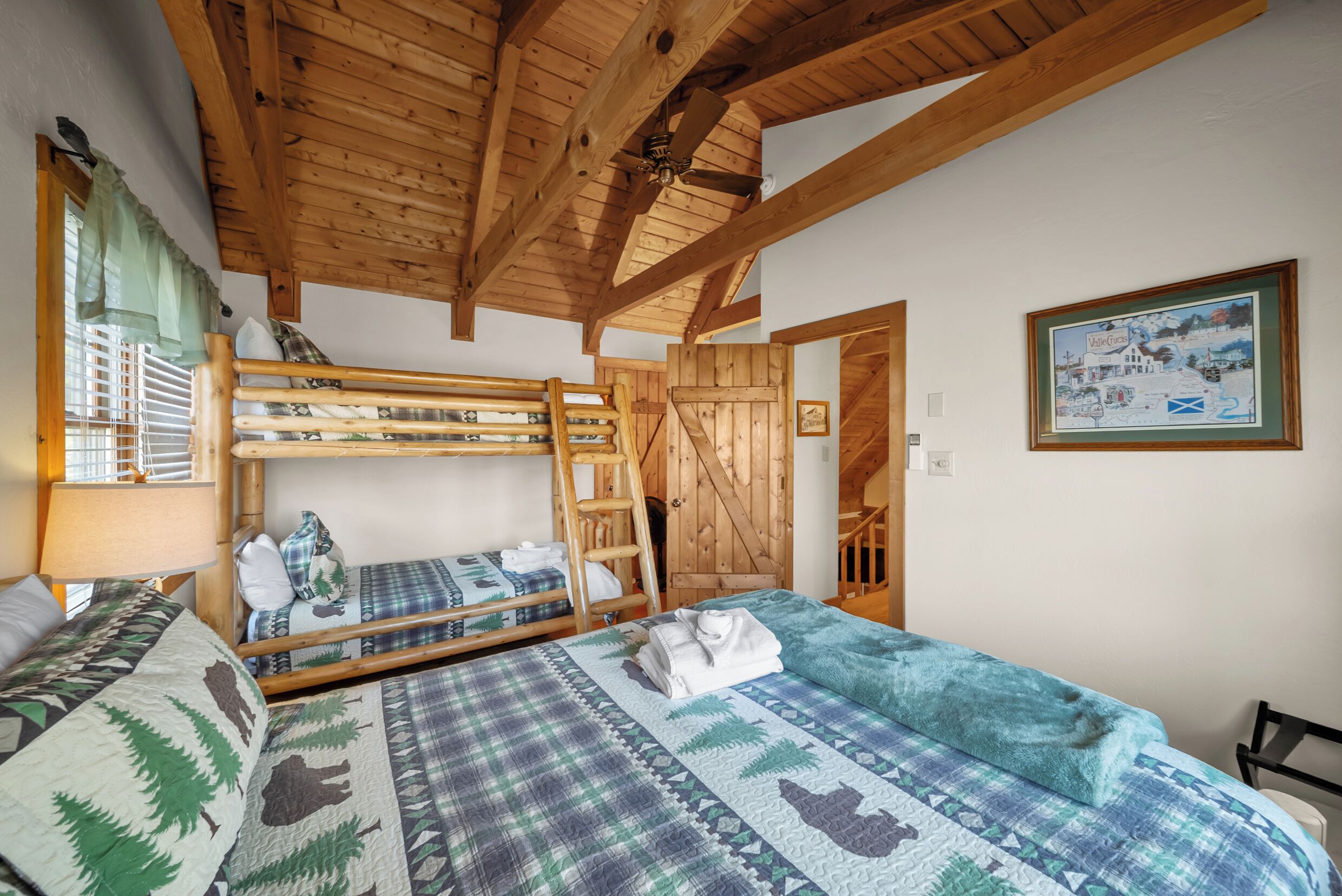 Une chambre avec un lit superposé, une échelle, un lit recouvert d’une couverture à motifs, un tableau encadré au mur et un plafond en bois.