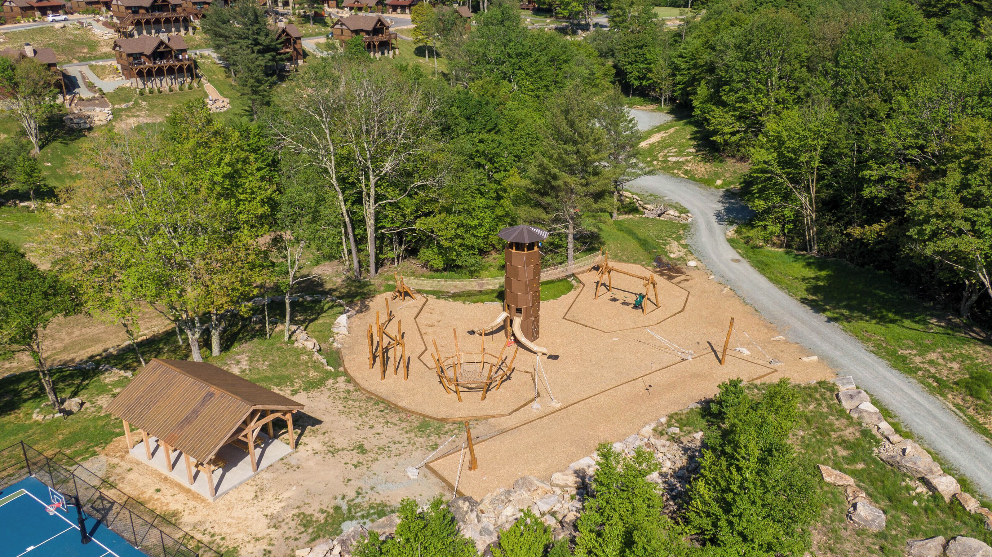 An aerial view of a park with a playground, a basketball court, and a small building.