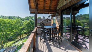 A wooden deck with a table and chairs, overlooking a lush green landscape. - Happy Camper at Eagles Nest (Banner Elk)