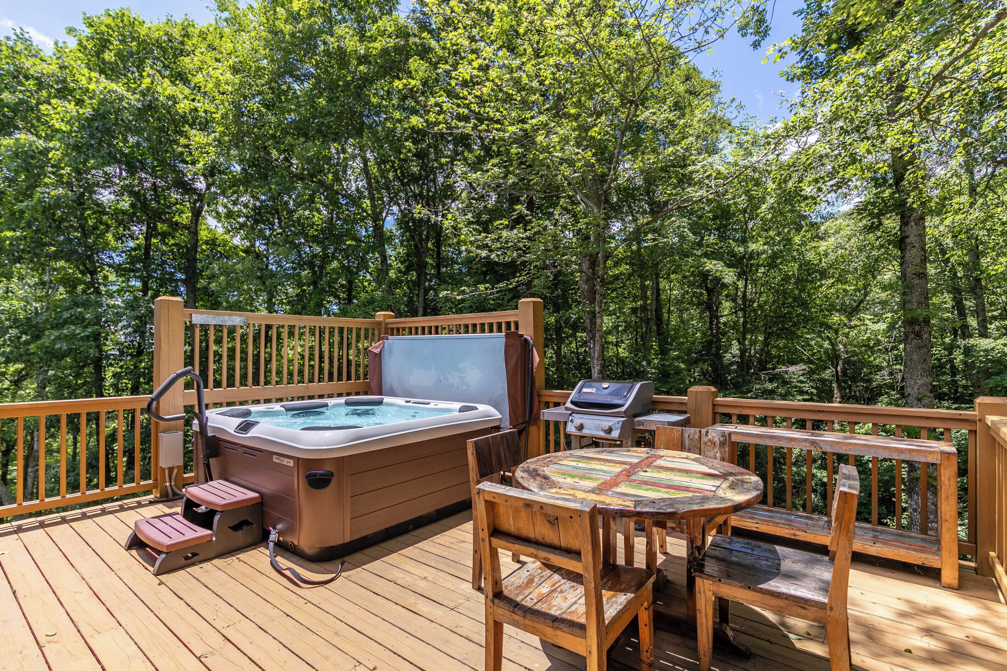 A wooden deck with a hot tub, a grill, and a table with chairs.