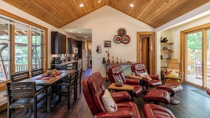 A spacious living area with a wooden ceiling, a dining table, leather chairs, and a view of the outdoors. - Carolina Wren Cottage (Blowing Rock)