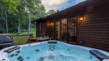 Un jacuzzi en una cabaña de madera con terraza, rodeado de árboles.