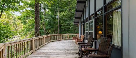 A wooden deck with chairs and a table, surrounded by trees.
