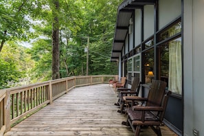 A wooden deck with chairs and a table, surrounded by trees.