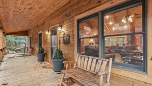 Een houten chalet met een veranda, een bankje en grote ramen die uitzicht bieden op het interieur.