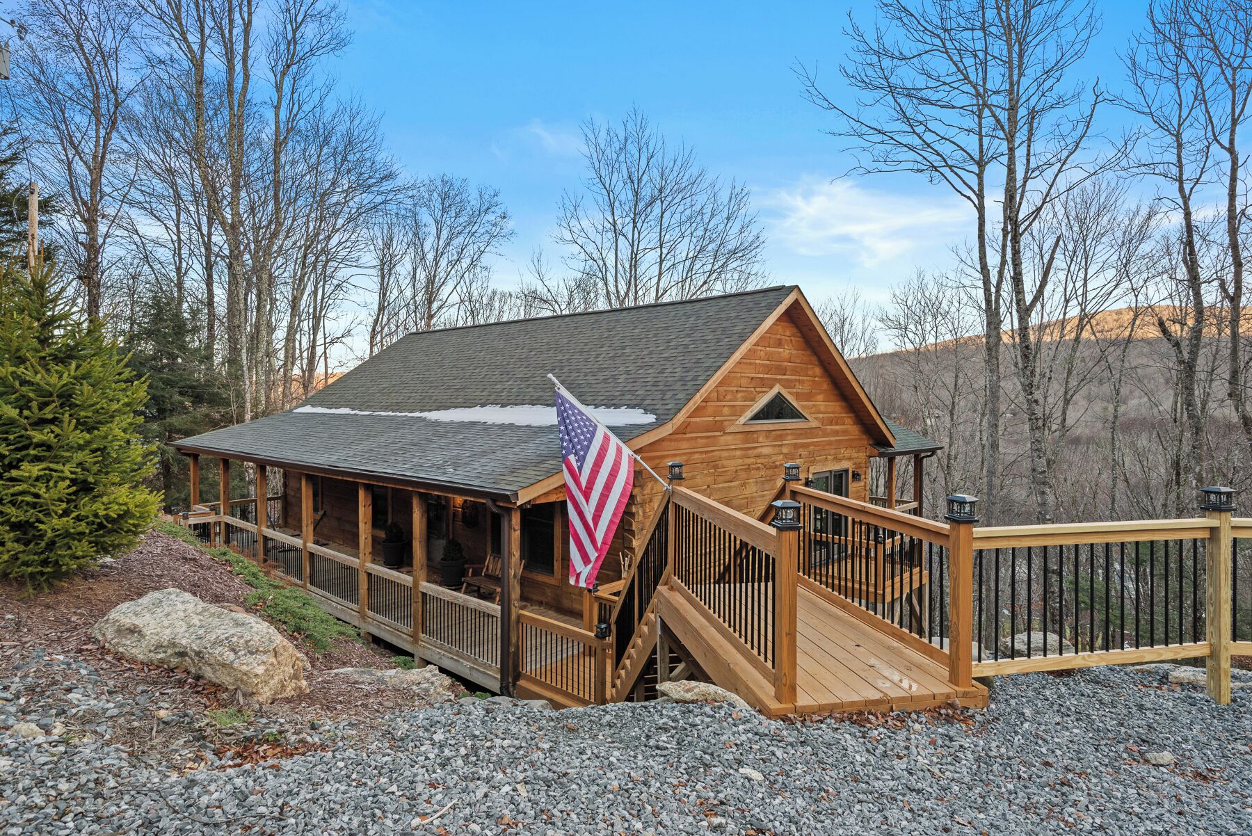 A wooden cabin with a deck, a flag, and a mountain backdrop.