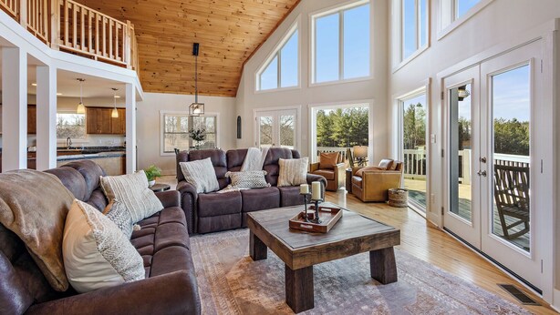 A spacious living room with a large sectional sofa, a coffee table, and a view of the outdoors through large sliding glass doors. - House Galini (Morganton)