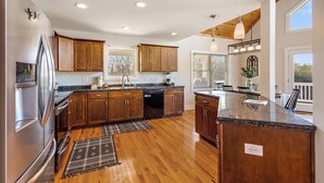 A modern kitchen with wooden cabinets, a stainless steel refrigerator, and a large island with a sink. - House Galini (Morganton)