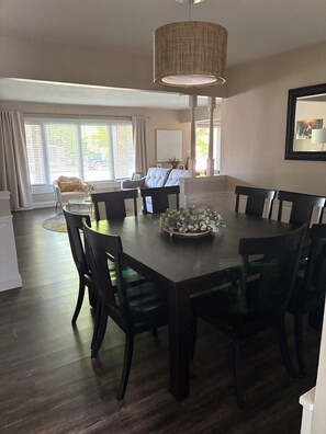 A dining area with a large table, chairs, a chandelier, and a view of the outdoors through large windows. - EAA Destination Home!  3 bedroom 2 1/2 bath and just 15 minutes from EAA! (Neenah)