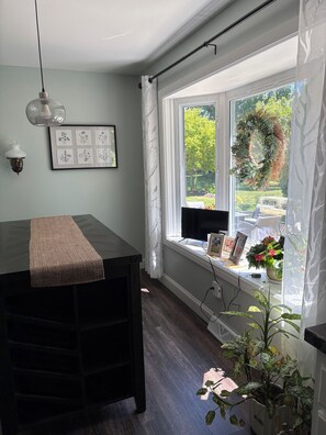 A room with a window seat, a table, a wall-mounted light fixture, framed botanical prints, and a potted plant. - EAA Destination Home!  3 bedroom 2 1/2 bath and just 15 minutes from EAA! (Neenah)