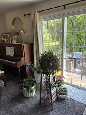 A piano, a mirror, a plant stand, and a window with a view of greenery. - EAA Destination Home!  3 bedroom 2 1/2 bath and just 15 minutes from EAA! (Neenah)