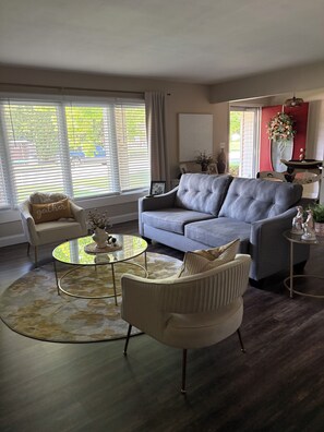 A living room with a grey sofa, a round glass coffee table, a white armchair, and a small side table with decorative items. - EAA Destination Home!  3 bedroom 2 1/2 bath and just 15 minutes from EAA! (Neenah)
