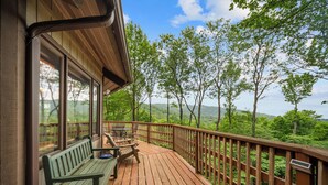 Eine Holzdar Terrasse mit einer Bank und einem Tisch, mit Blick auf ein bewaldetes Gebiet.