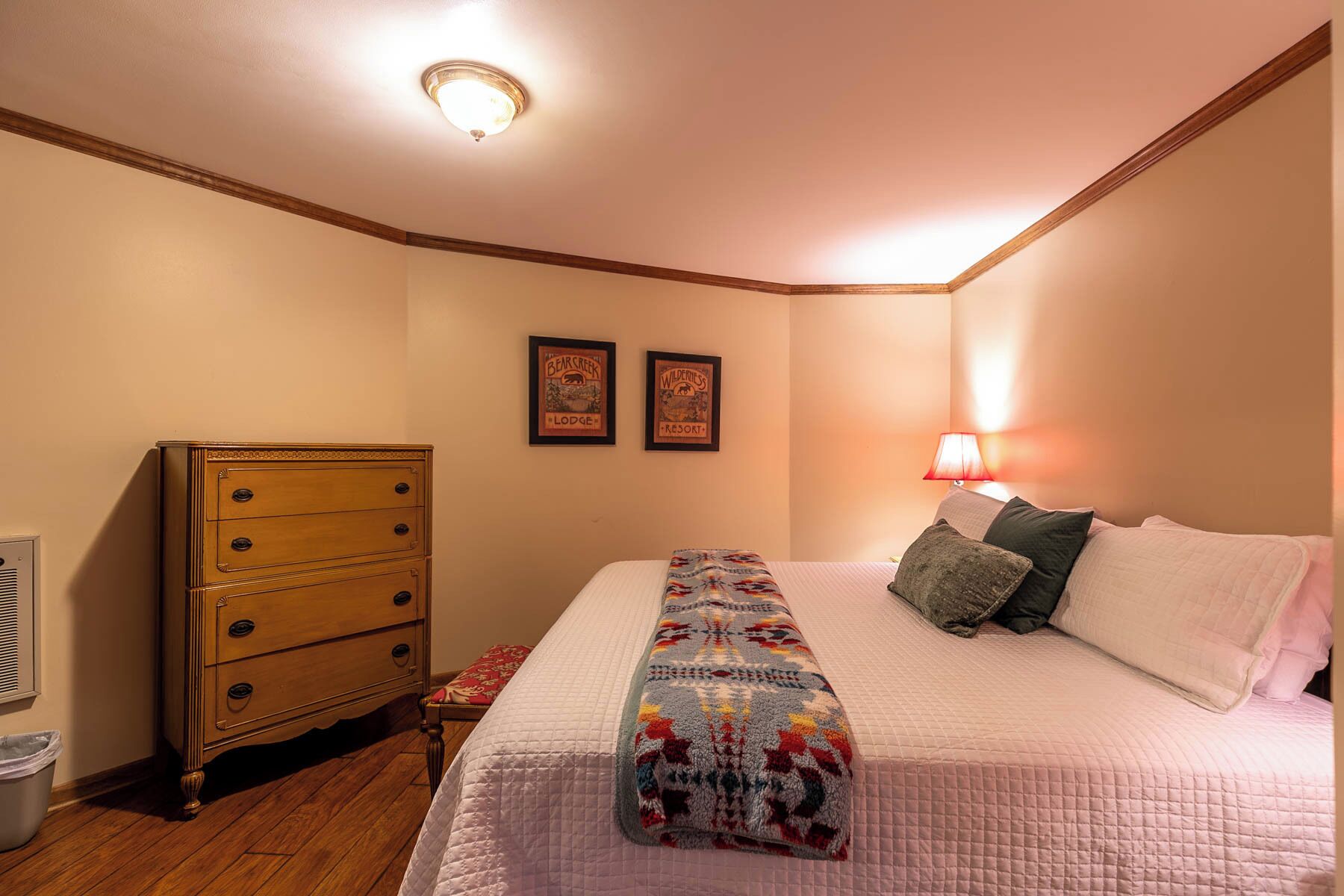 A bedroom with a wooden dresser, a bed with a patterned quilt, and two framed posters on the wall.