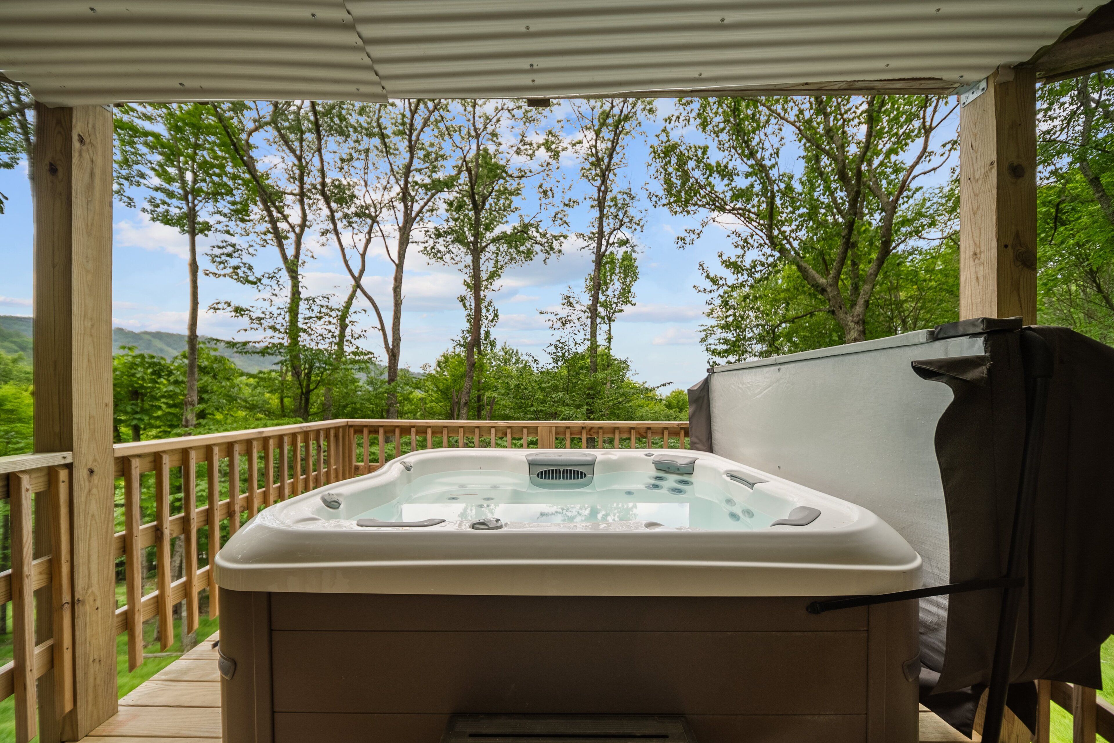 Ein Whirlpool auf einer Holzterrasse mit Blick auf Bäume und Hügel.